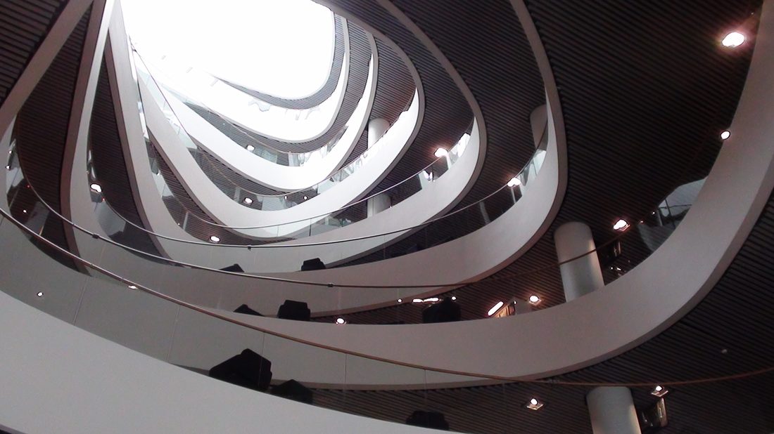 Interior atrium of a university library with layered curved balconies and skylight, representing the academic environment students adapt to when studying abroad.